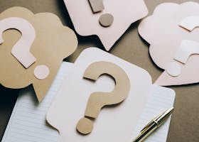 Artistic paper question marks on an open notebook with a pen, symbolizing curiosity and creativity.